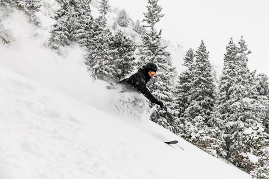 Male Skier In Black Ski Suit , Helmet And Goggles Sliding Down Snow-covered Slopes On Skis