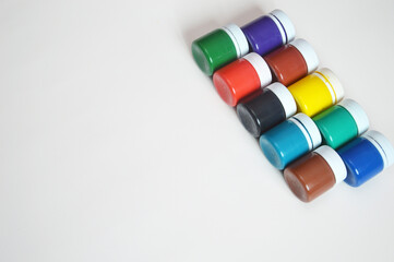 Closed jars with gouache of different colors standing in a row on a white background. Hobby, drawing, painting.