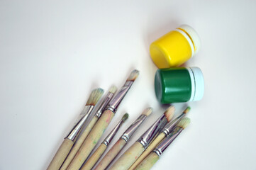 A set of brushes with wooden handles and bristle bristles lying with cans of gouache yellow and...