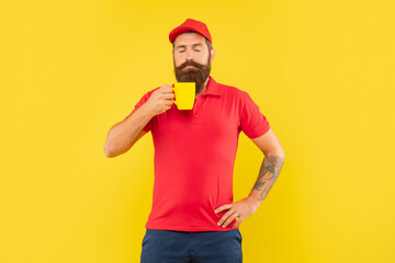 Serious bearded man smelling hot beverage with closed eyes holding cup yellow background, coffee