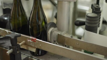Close-up automated corking machine in wine factory with glass bottles passing. Process of beverage packing and labeling indoors in winery. Industrial concept