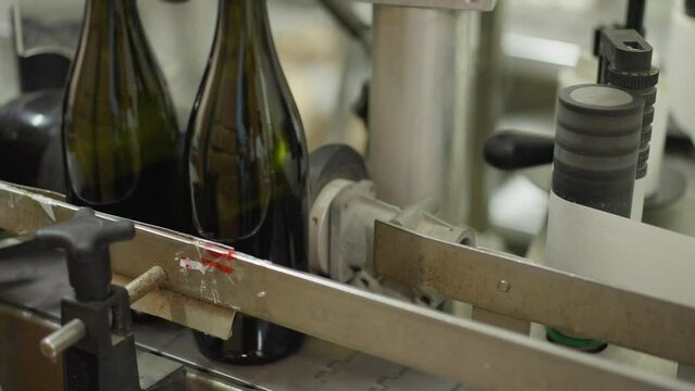 Close-up automated corking machine in wine factory with glass bottles passing. Process of beverage packing and labeling indoors in winery. Industrial concept
