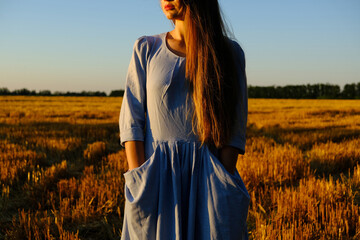 Obraz premium Escapism, getting away from it all, mental health, Stress resilience. Alone Young woman in linen dress walking on mowed wheat field at sunset. Peaceful woman with long hair spending time in nature