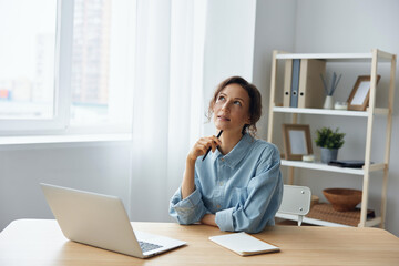 Dreaming thoughtful cheerful smart gorgeous pensive curly businesswoman think about weekend smiling looks aside using laptop in office. Modern Job Remote Work concept