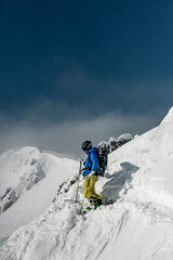 Fototapeta na wymiar Skier man in goggles, helmet and blue and yellow ski suit doing ski touring in winter mountai