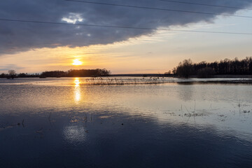 Spring flood. Sunset over the river, dramatic sky over the horizon. The sun is reflected in the water. Bright spring landscape with a river. Flooding of agricultural land.