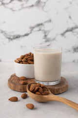 Glass of almond milk with nuts on a wooden board on a light background