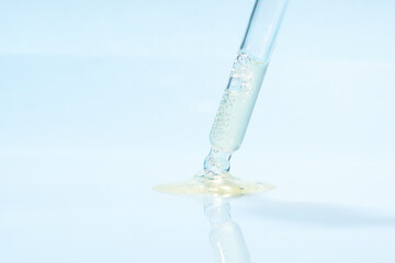 Front view of transparent pipette dropper with light yellow drop of serum cosmetics, oil, gel ou cream on blue background and bubbles of air. Minimal beauty concept, macro closeup with copy space