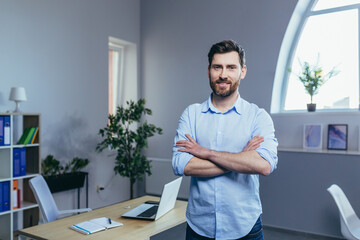 Successful businessman with arms crossed looking at camera and smiling man at work in office