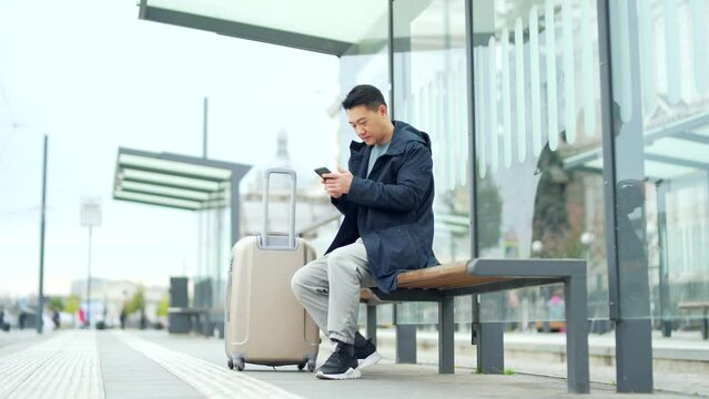 Tourist at the bus station, orders a taxi using the application on the phone, Asian male traveler book accommodation online for business travel a modern train public transport in the city