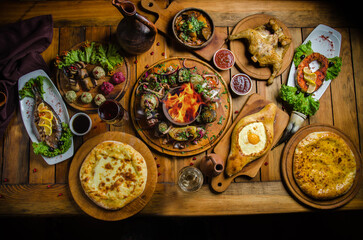 Georgian cuisine. A large set table of different dishes for a large company. Pkhali, eggplant roll, tapaka chicken, kebab, ajapsandal, khachapuri and grilled fish. Top view on a large wooden table.