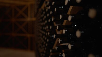 Live camera moves along rows of corked wine bottles stacked in wine cellar indoors. Expensive high-quality beverage in bodega in darkness. Luxury and winemaking concept