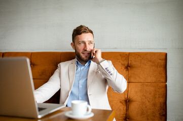 A smiling businessman is sitting in a cafe and talking on his phone. A new work week with a lot of...