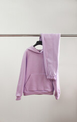 teen clothes design. violet oversize hoodie with violet warm pants on the silver hanger on the white wall background. minimal fashion concept