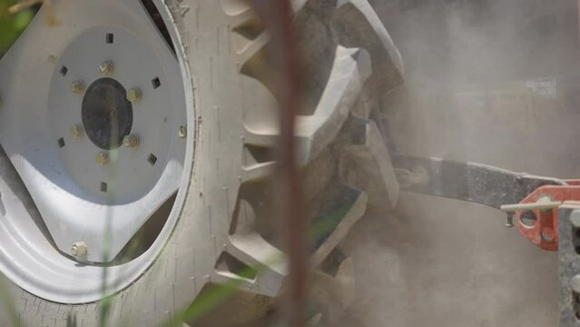 Close-up large industrial vehicle wheel rolling in slow motion in sunshine raising dust. Side view agricultural machinery working on field outdoors on sunny summer day on Cyprus