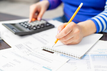 Woman using calculator for calculate domestic bills at home, doing paperwork for paying taxes