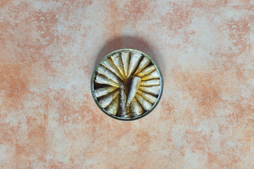 Overhead view of a large round sardine tin on a pastel marble texture background. Canned food and fish.