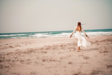 Model in boho style in a white long dress and silver jewelry on the beach. Her hair is braided, and...