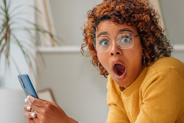 girl at home amazed and surprised looking at mobile phone
