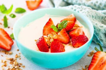 Yogurt with granola and strawberry in blue bowl at light stone table. Close up.