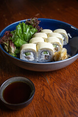 Side view of Japanese sushi roll served with ginger and wasabi on dark blue glass plate