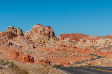 Overton, Nevada, USA - February 24, 2010: Valley of Fire. Up and down goes the black asphalt road with yellow divider between beige-red rock formations under blue sky over dry desert floor.