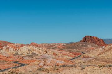 Naklejka premium Overton, Nevada, USA - February 24, 2010: Valley of Fire. Long meandering black asphalt road meandering through very wide landscape of red and beige rock over dry desert floor under blue sky.