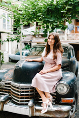 The girl, woman is sitting on ancient, vintage car. Young female during a walk the street of old city, town, outdoors. The concept holiday and travel.