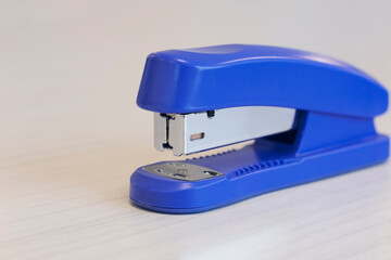 A blue stapler on wooden office desk. Close up stapler