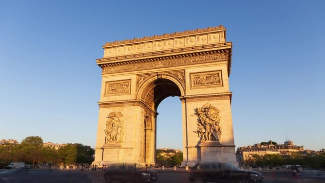Paris France: Triumphal Arch of the Star (Arc de Triomphe de l'&Eacute;toile) - famous landmark and tourist attraction at sunrise. Traffic on the street in a sunny morning under clear blue sky.