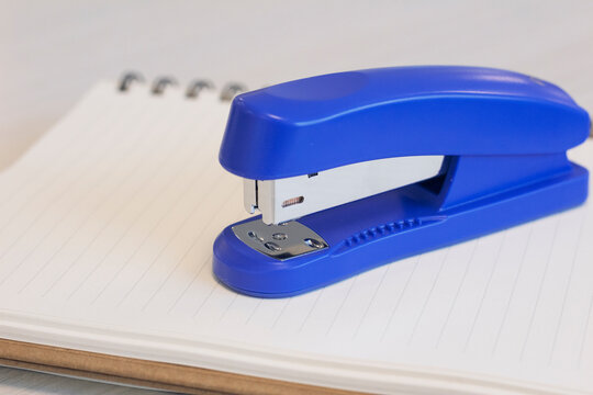 A blue stapler and a notebook on wooden office desk. Close up stapler