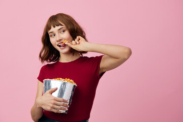 Smiling cheerful pretty cute redhead lady in red shirt with popcorn ready to watch movie posing isolated on over pink studio background. Copy space Banner. Fashion Cinema concept. Entertainment offer