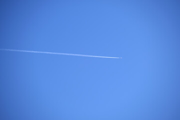 Distant passenger jet plane flying on high altitude on clear blue sky leaving white smoke trace of contrail behind. Air transportation concept