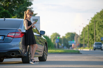 Stylish woman driver standing near her vehicle talking on cellphone on city street in summer