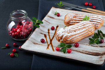 Cream eclairs choux pastries served with fresh cranberries on a handmade ceramic plate. Profiterole cupcakes - 501634153