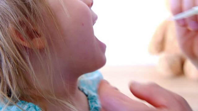 close-up of male hands, doctor, pediatrician examines oral cavity of small patient, toddler, small child, blonde girl looks trustingly at man, concept treating children, length of frenum of tongue