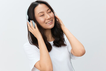 Naklejka premium Relaxing happy cute Asian young female in white basic t-shirt touch headphones closing eyes posing isolated on over white studio background. The best offer for ad. Favorite Music App Ad concept