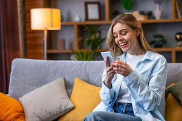 Emotional woman with mobile phone reading message on sofa in room