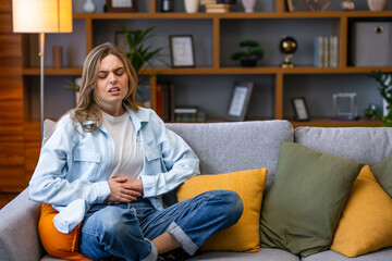 Young woman frowning having stomach ache sitting on the couch