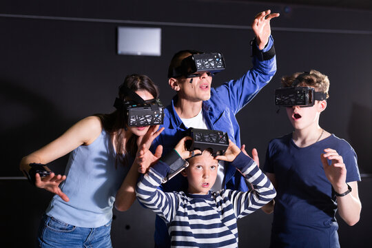 Modern cheerful family with two teen sons wearing virtual reality goggles playing video games together