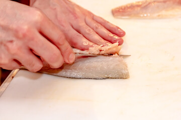 The process of butchering pike fish for frying in a pan. Elderly woman's hand cut fish on a cutting kitchen board