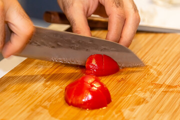 Chef slicing fresh ripe tomatoes on a chopping board surrounded by ingredients for Italian and Mediterranean cuisine in a close up on his hands