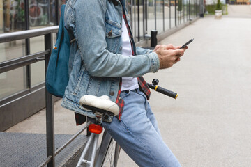 Young adult leaning on a bicycle using a smartphone in the city