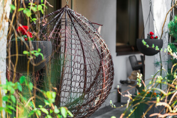 Close-up of a hammock chair in the shape of a wicker cocoon, a garden swing hanging from a frame on...