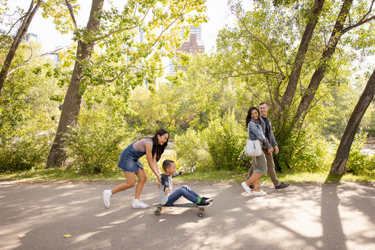 Sister Pushing Brother On Skateboard In Sunny Park