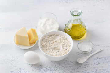 Ingredients for cooking traditional Italian biscotti cheese croutons: wheat flour, natural yogurt, egg, hard cheese, olive oil, salt and baking powder on a light gray background