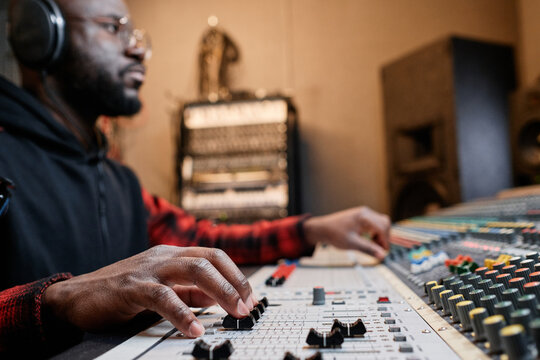 African American music producer working in record studio adjusting mixing console settings, selective focus shot