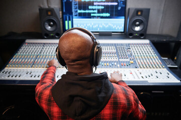 Rear view shot of unrecognizable Black sound engineer producing recording in studio adjusting sound...
