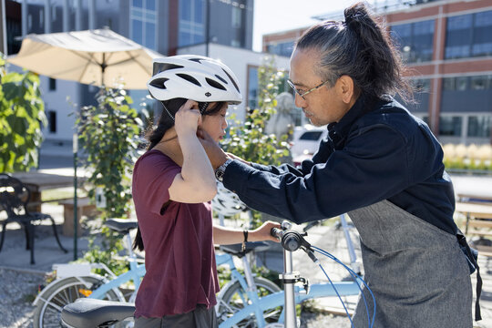 Father helping daughter with Down Syndrome put on bicycle helmet
