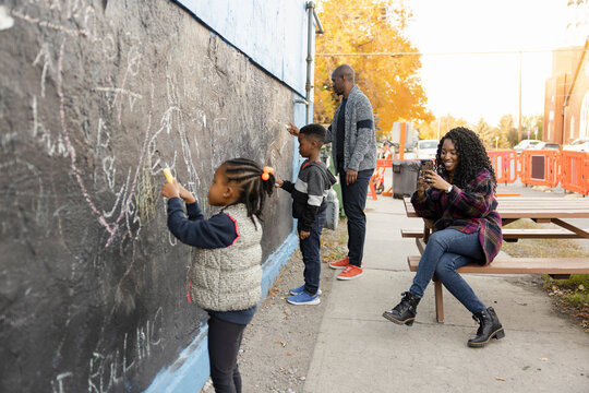 Mother photographing kids drawing on wall with chalk